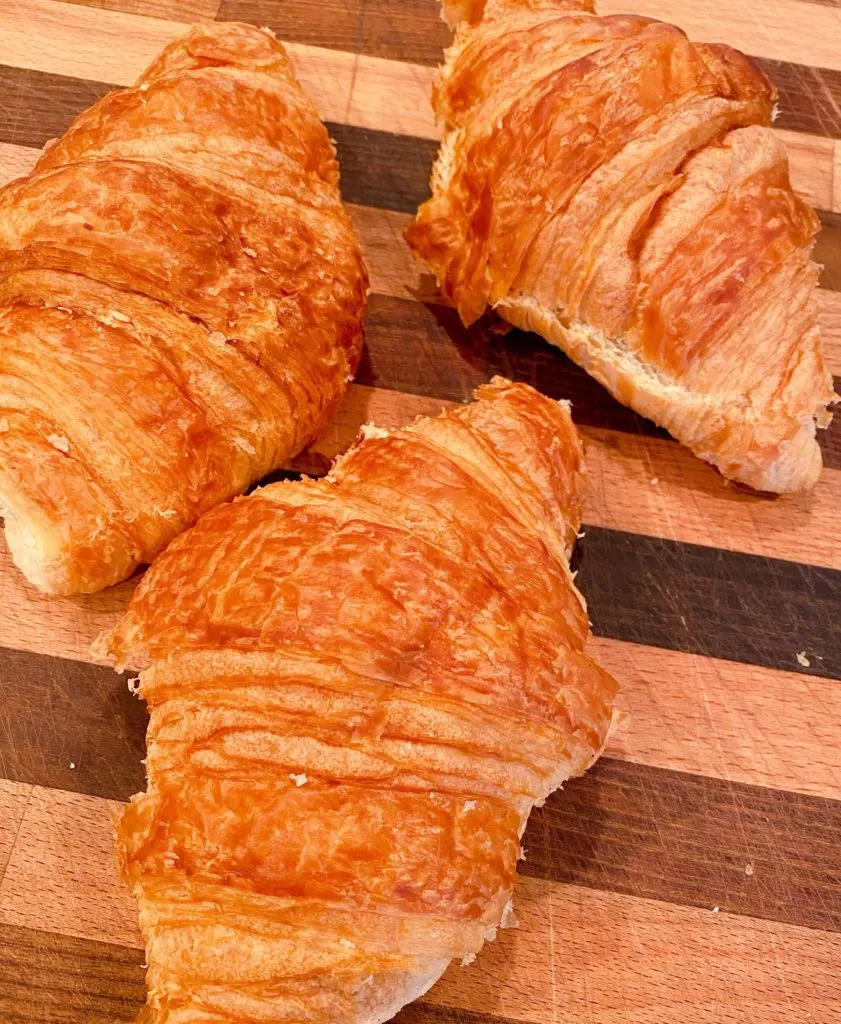 Three store bought croissants on a cutting board.