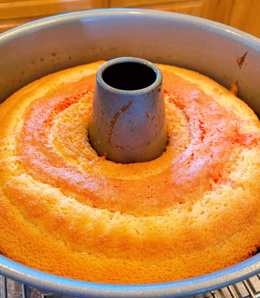 Baked cake in bundt pan cooling on cake rack.