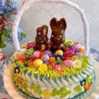 Easter Basket Cake on a cake stand with flowers in the background.