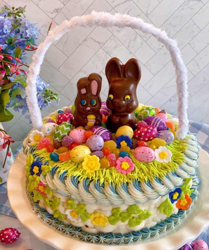 Easter Basket Cake on a cake stand with flowers in the background.
