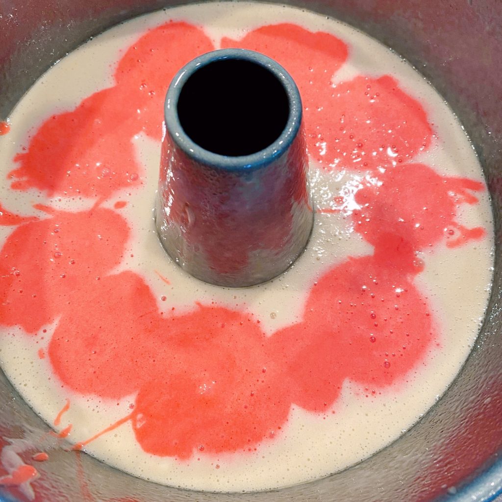 Adding strawberry cake batter to vanilla cake batter in the bundt pan.