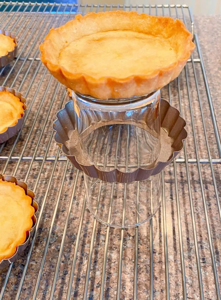 Shortbread crust tart pan on top of a glass with the outer sleeve slide down the glass and the tart crust on top.