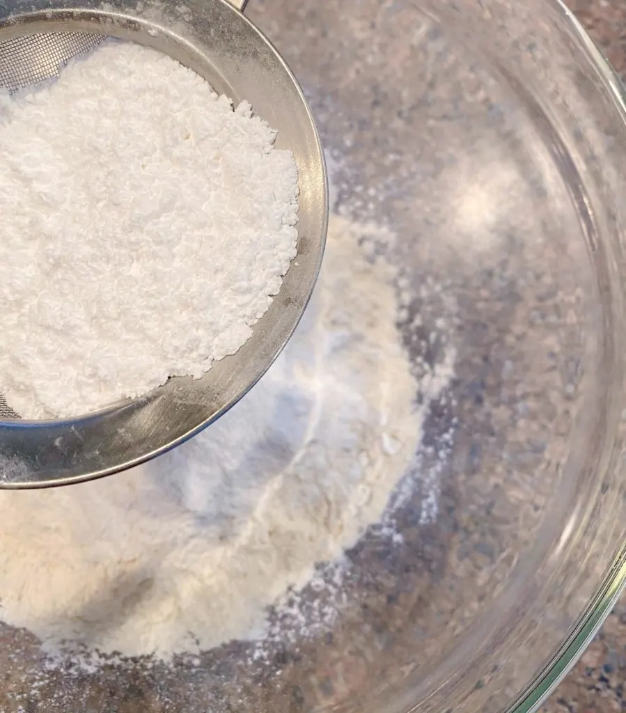 sifting confectioners sugar into flour in medium glass bowl.