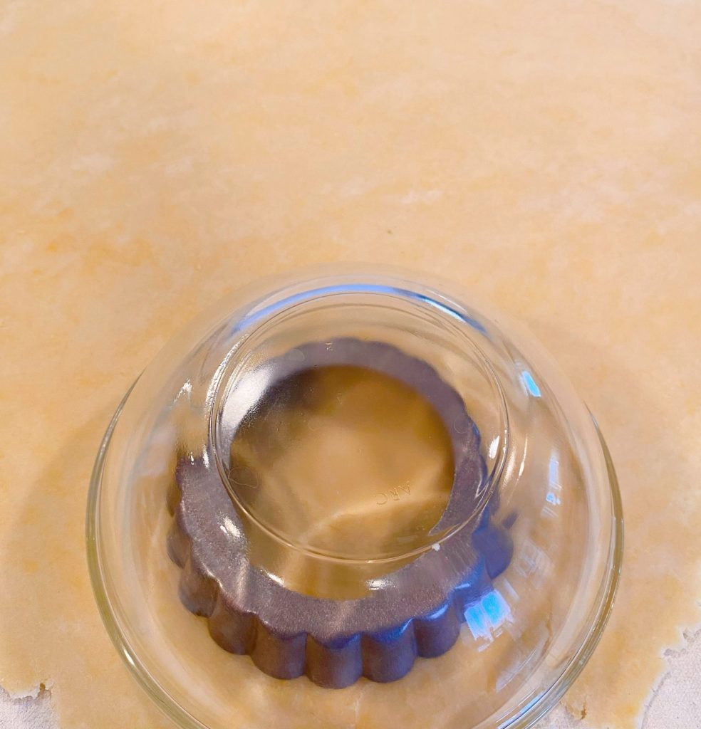 Cutting out tartlet crust for tarts. Tartlet pan face down on the dough with a slightly larger bowl on top to use as a guide.