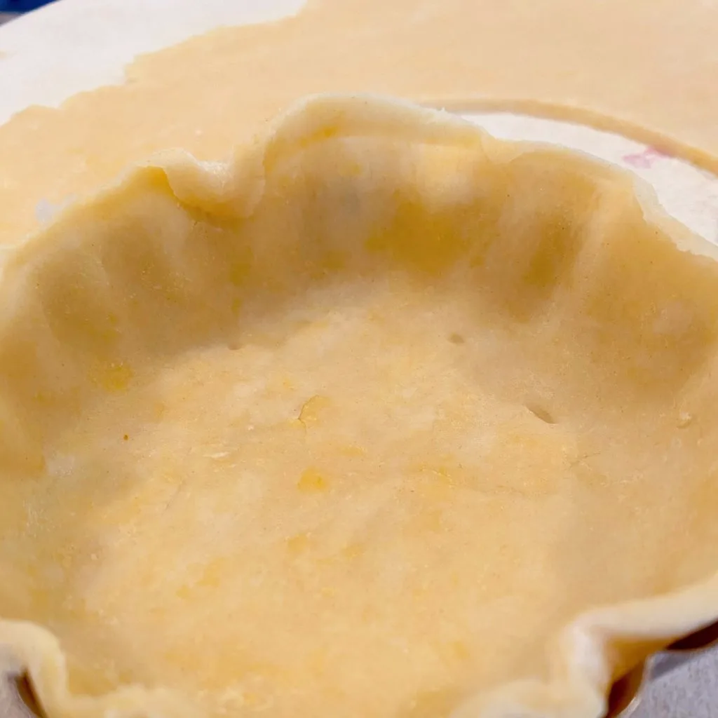 Tart crust on small tartlet pan with dough hanging slightly over the edge.