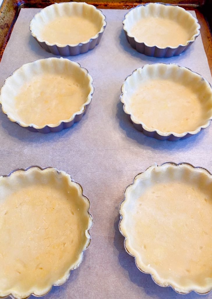 6 tart crust lined pans on a baking sheet lined with parchment paper.