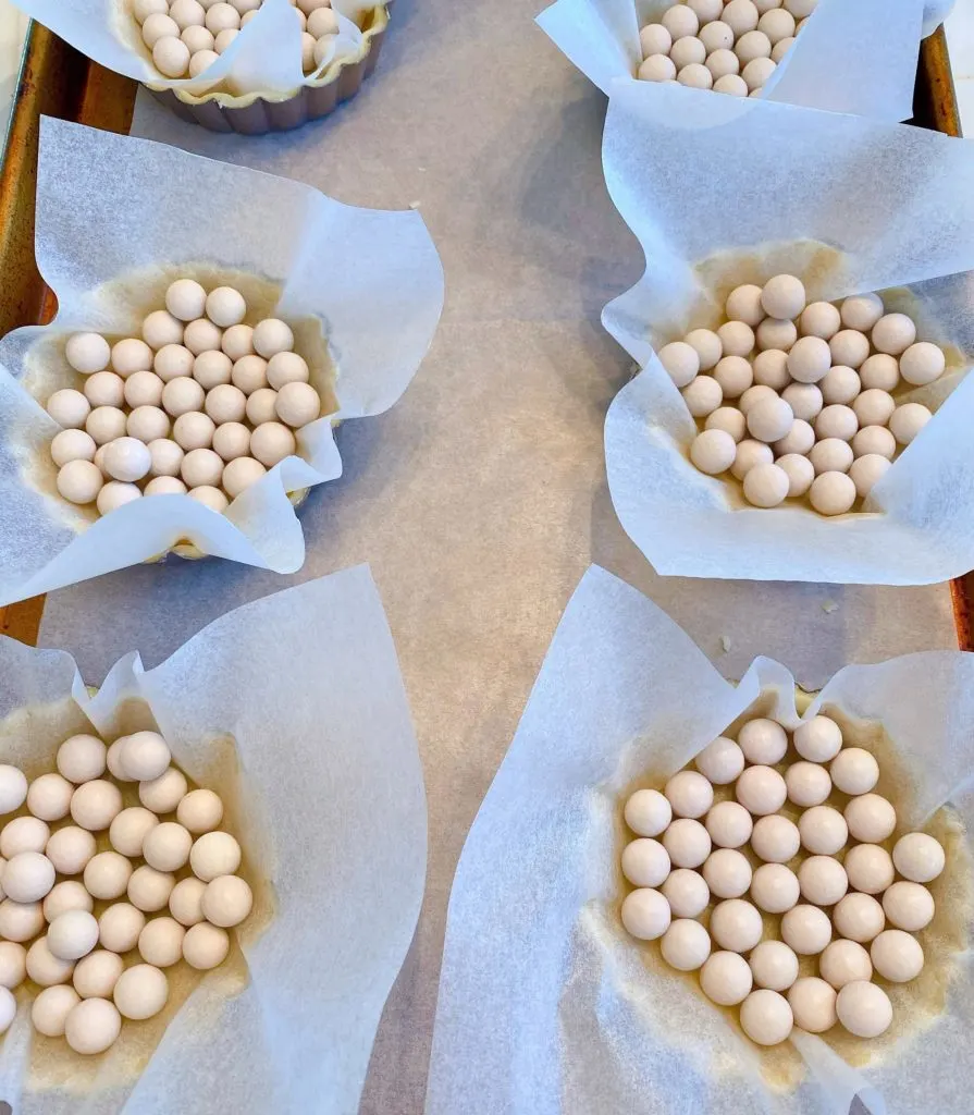 Shortbread crusts in tart pans lined with parchment and ceramic baking beads. 