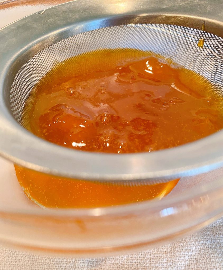 Jam in a sieve straining into a smaller bowl.