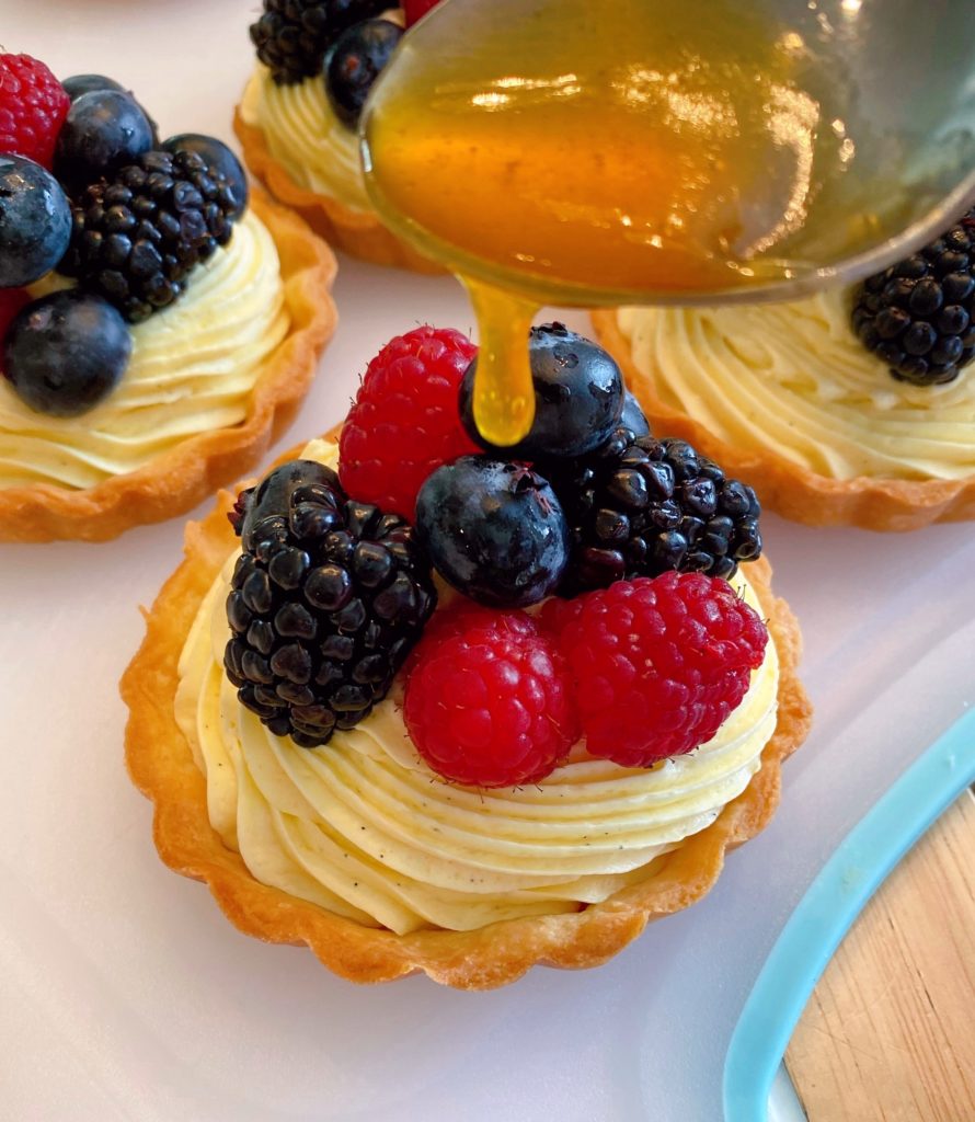 Pouring apricot glaze over the top of the berries.