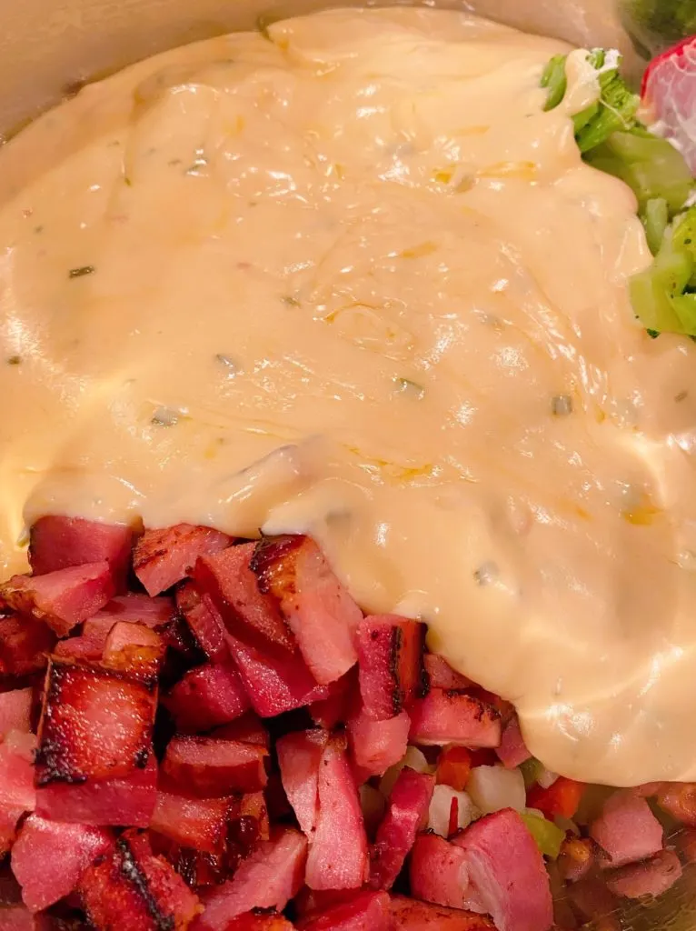 Adding cheese sauce to casserole ingredients in large bowl.