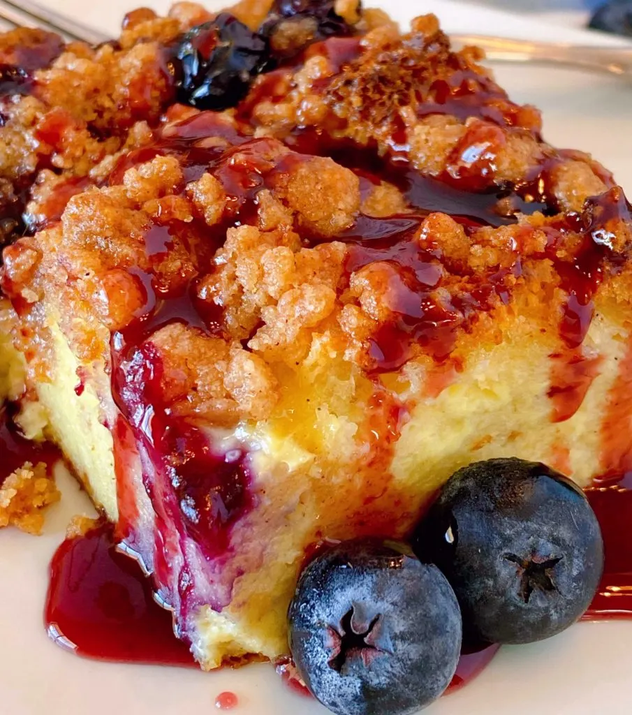 Close up shot of a slice of blueberry french toast bake drizzled with mixed berry syrup.