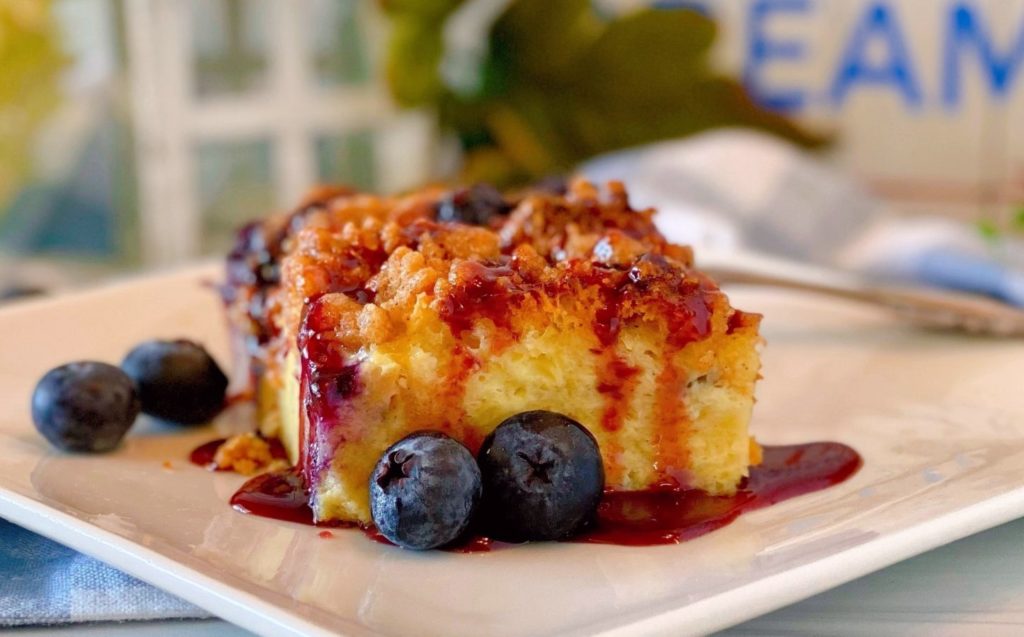 Slice of Blueberry French Toast Bake Recipe on a white plate drizzled with berry syrup.