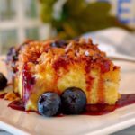 Slice of Blueberry French Toast Bake Recipe on a white plate drizzled with berry syrup.