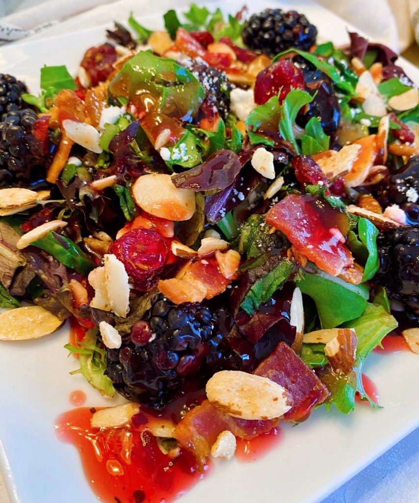 Close up photo of a serving of Spring Berry Feta Salad on a square white salad plate with raspberry vinaigrette.