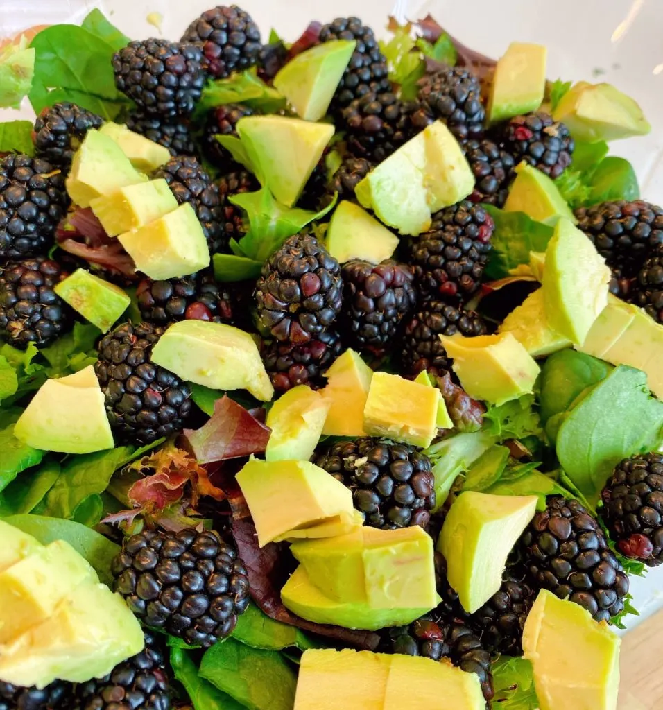 Adding Blackberries and Diced Avocado to Salad Greens in large salad bowl.