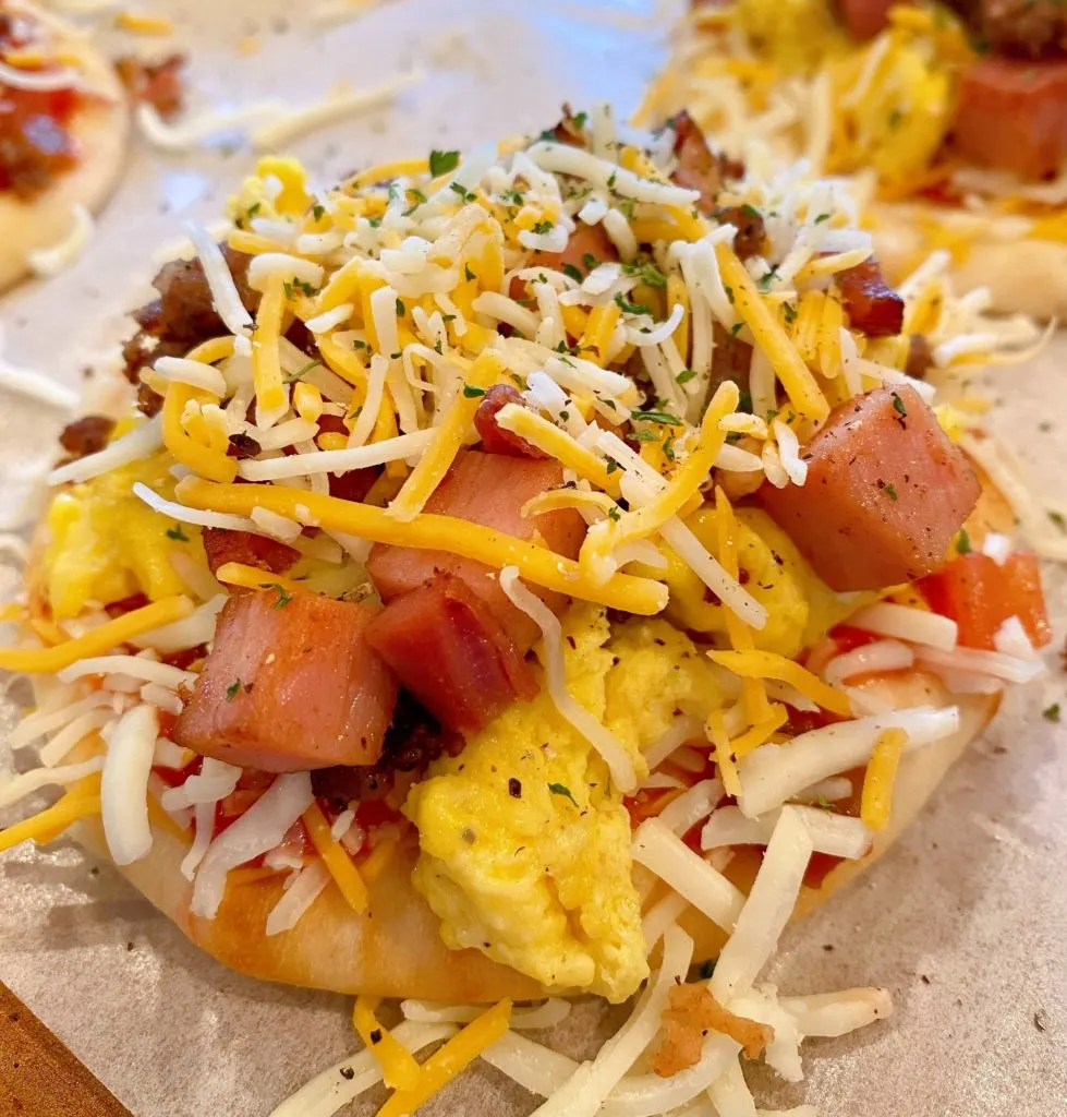 Topping pizzas with cheese and bacon with parsley.