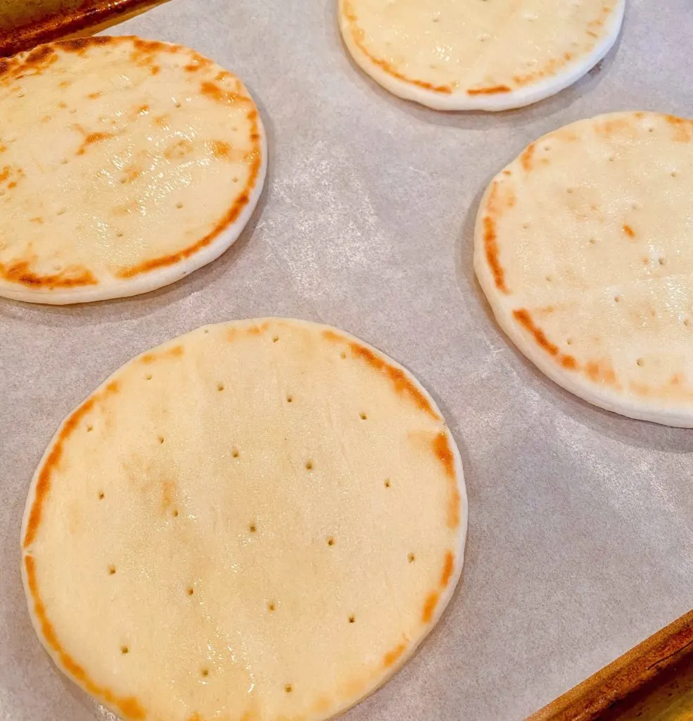 Naan rounds on parchment paper on baking sheet.