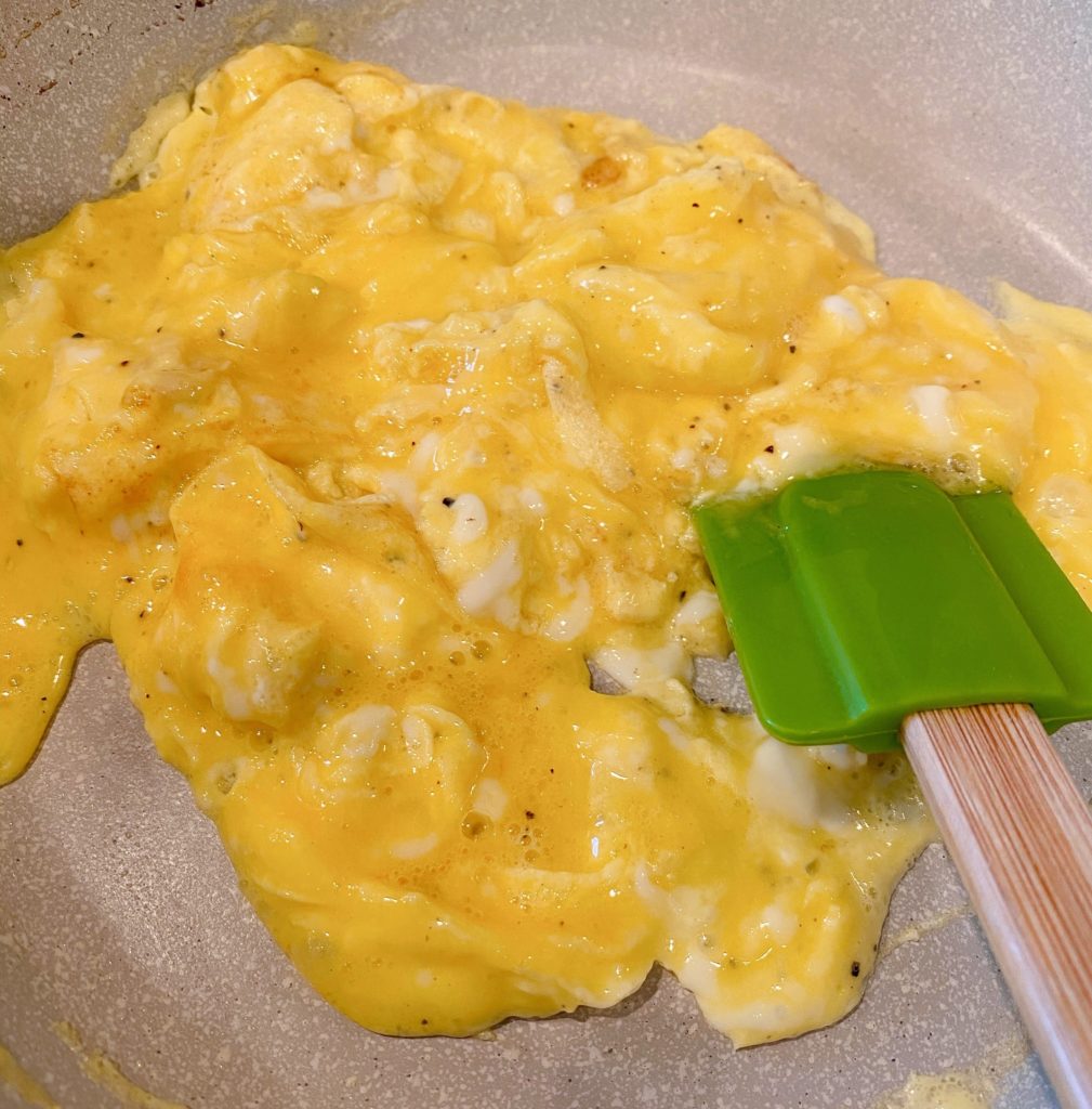 Scrambling the eggs in a skillet using a rubber spatula.
