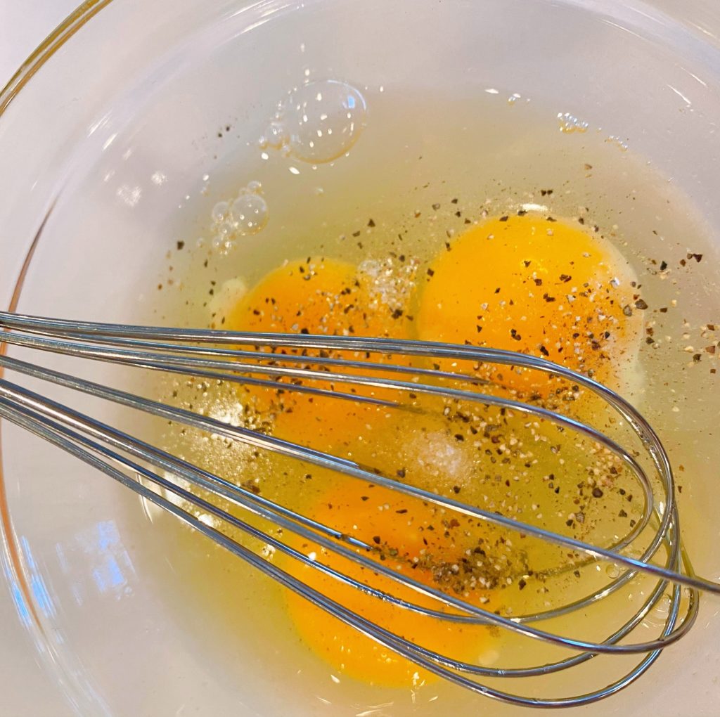 Three large eggs cracked and in a bowl with salt and pepper ready to be whisked. 
