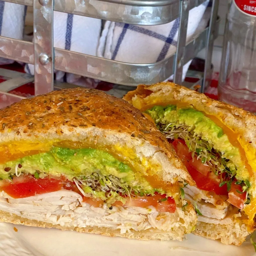Close-up of Turkey Sandwich on white plate with wire basket in the background.