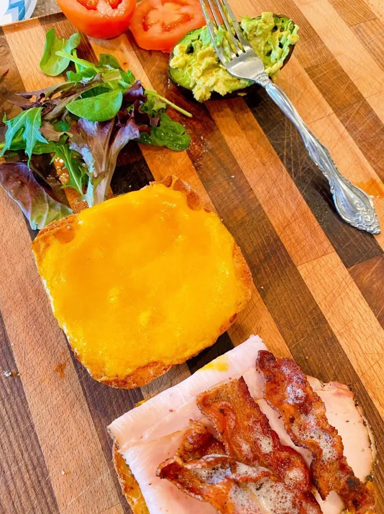 Sandiwch toppings on a cutting board with hot sandwich on the cutting board too.