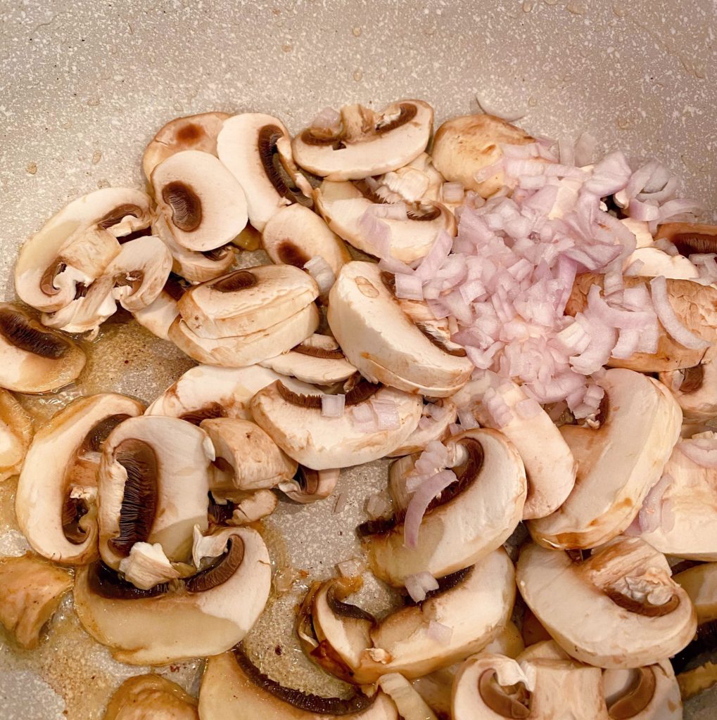 Sliced mushrooms and scallion in pan.