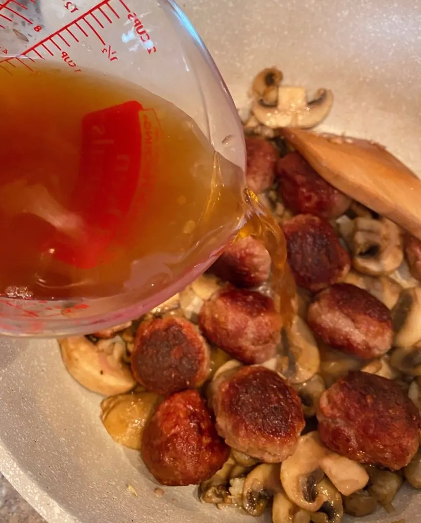 Adding beef broth to pan with meatballs and mushrooms.