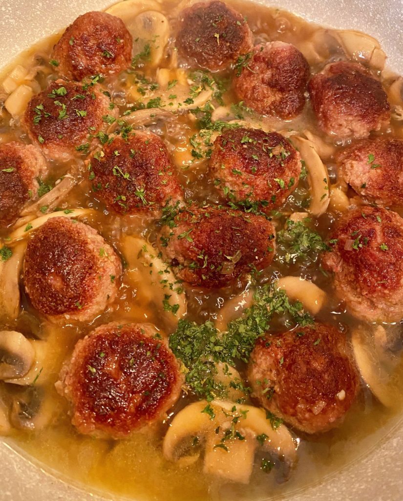 Meatballs and broth simmering in large pan.