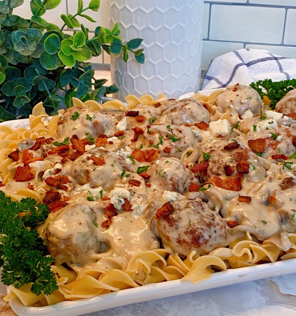 Creamy Bacon & Ground Beef Meatballs in a creamy mushroom sauce over egg noodles on a white serving platter with parsley as a garnish.