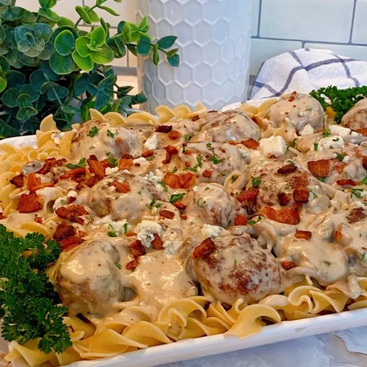 Creamy Bacon & Ground Beef Meatballs in a creamy mushroom sauce over egg noodles on a white serving platter with parsley as a garnish.