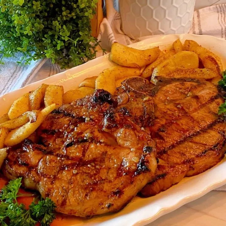 Grilled Honey Garlic Bone-in Pork Chops with fried apple slices on a white serving platter.