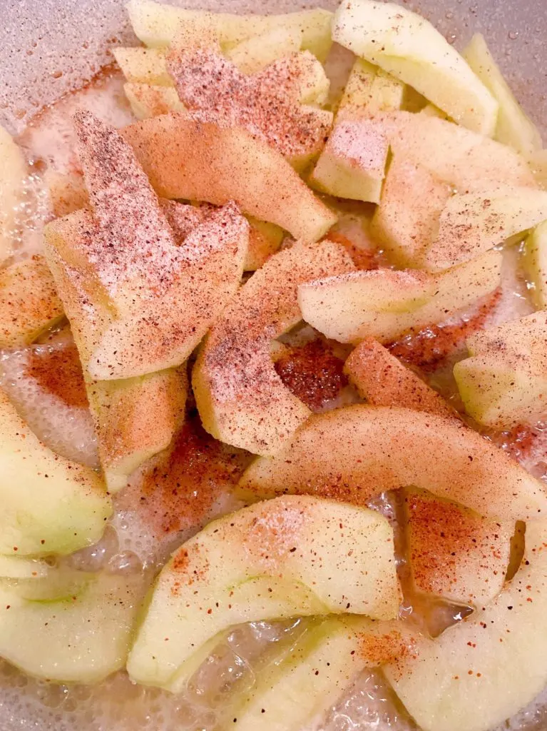 Raw apple slices in a skillet with butter and cinnamon sugar.