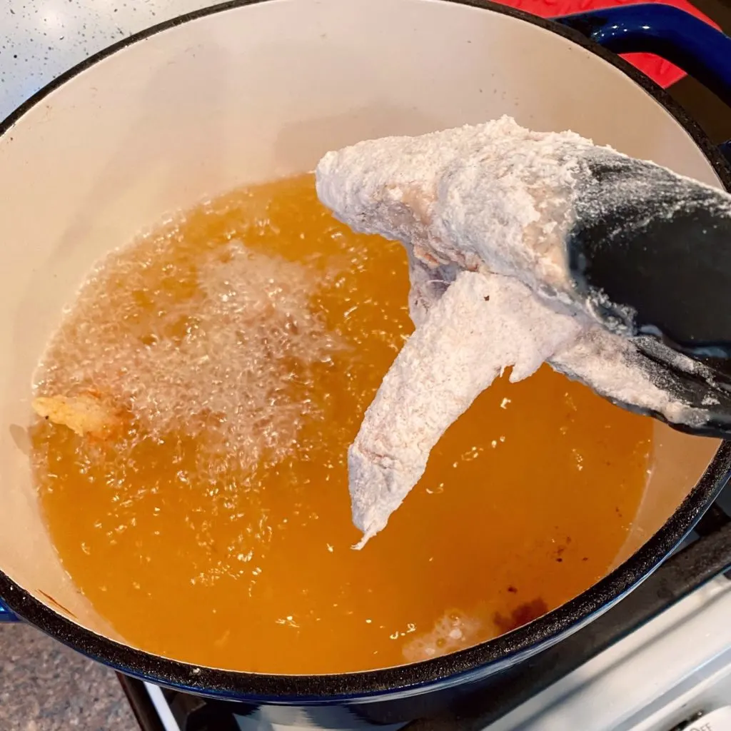 Placing chicken in hot oil to fry.