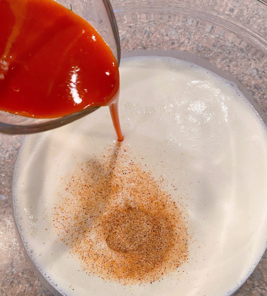 Large bowl with buttermilk, crole seasoning, and buffalo sauce for chicken.