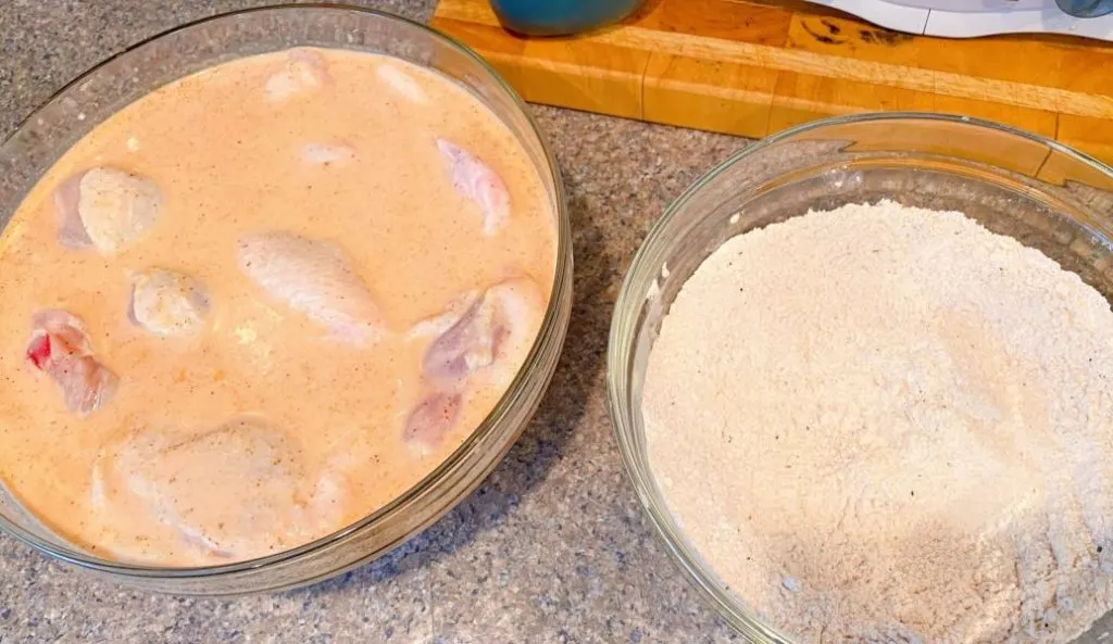 Chicken and dry flour dredge next to each other on the counter.