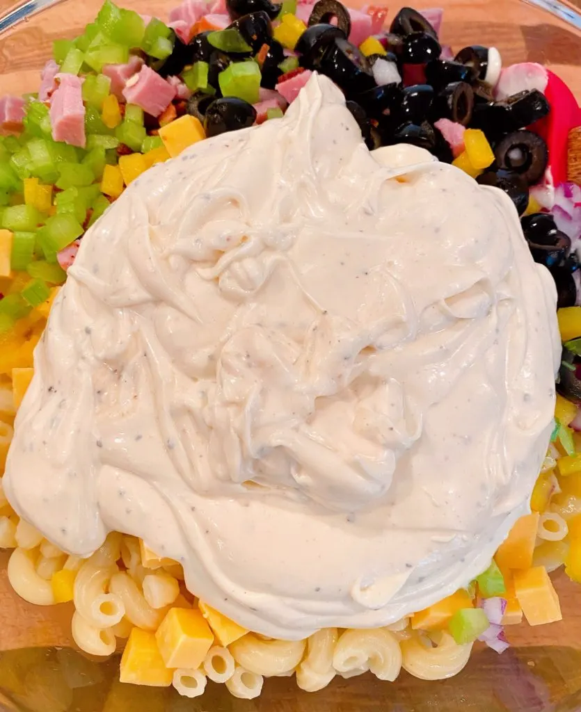 Adding creamy dressing to macaroni salad ingredients.