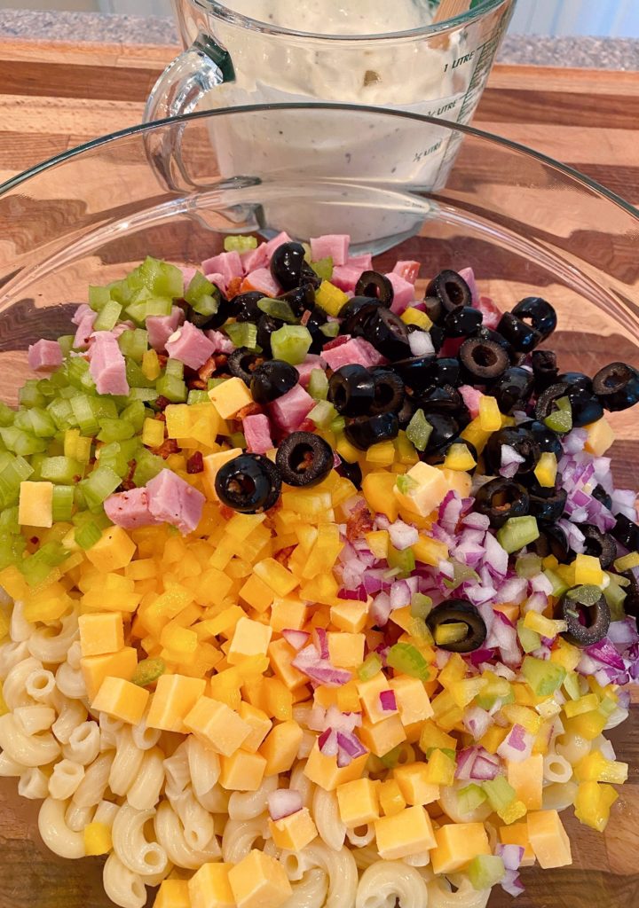 Adding salad ingredients to the macaroni.