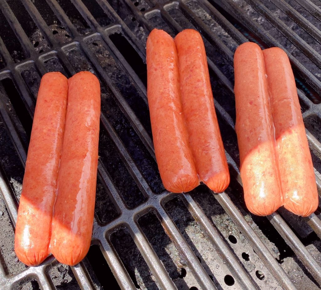 Sliced hot dogs on the grill cooking.