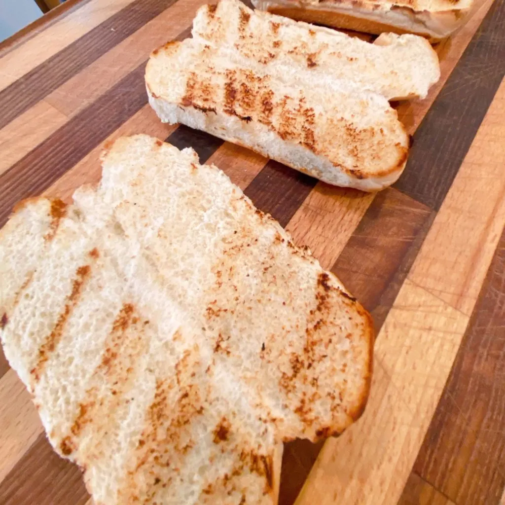 Two Toasted Hot Dog Buns on a cutting board.