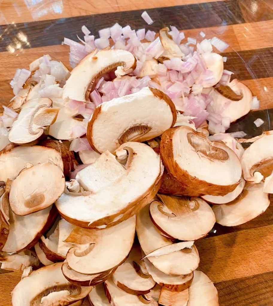 Sliced mushrooms and minced shallots on a cutting board.