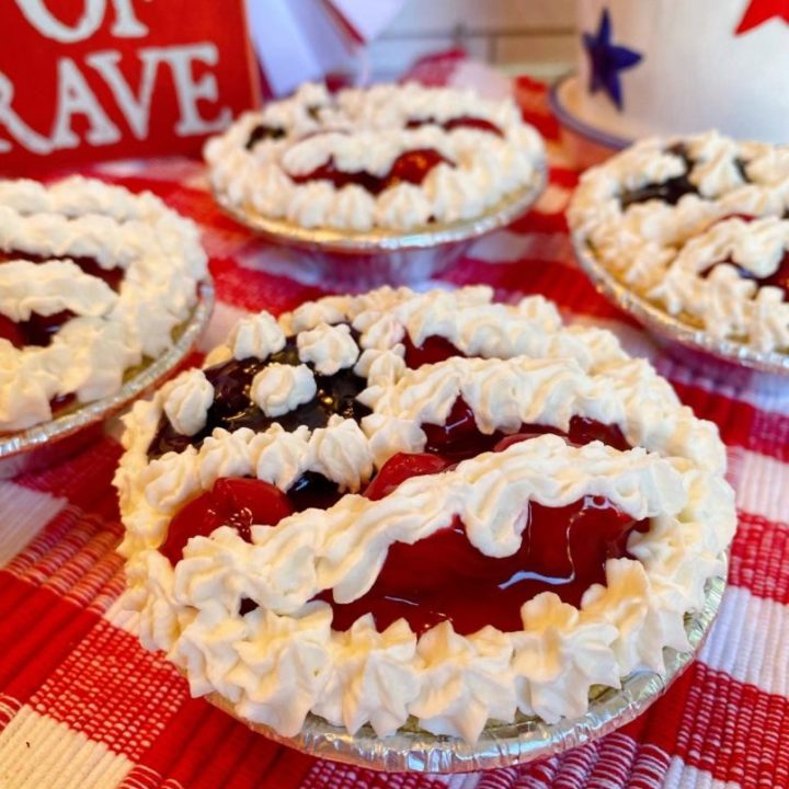 Mini No Bake Patriotic Cheesecake Pies with cherry and blueberry pie filling decorated like a flag on a red and white plaid cloth.