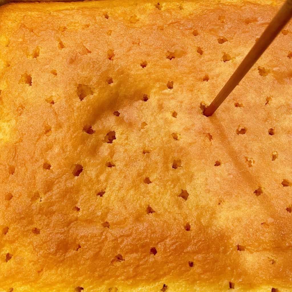 Baked cake being poked with chop stick to create holes all over the top of the cake.