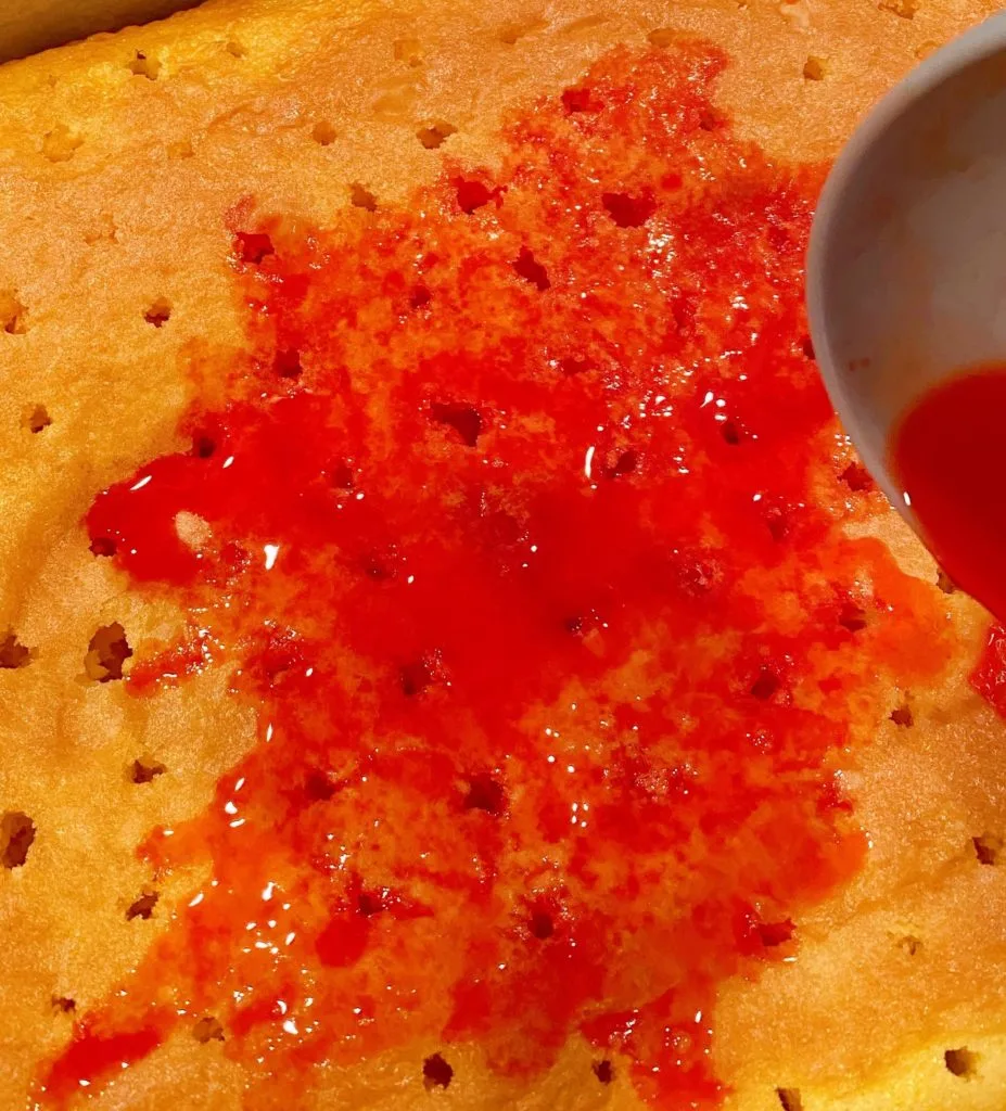 Spooning jello into holes in the top of the cake.