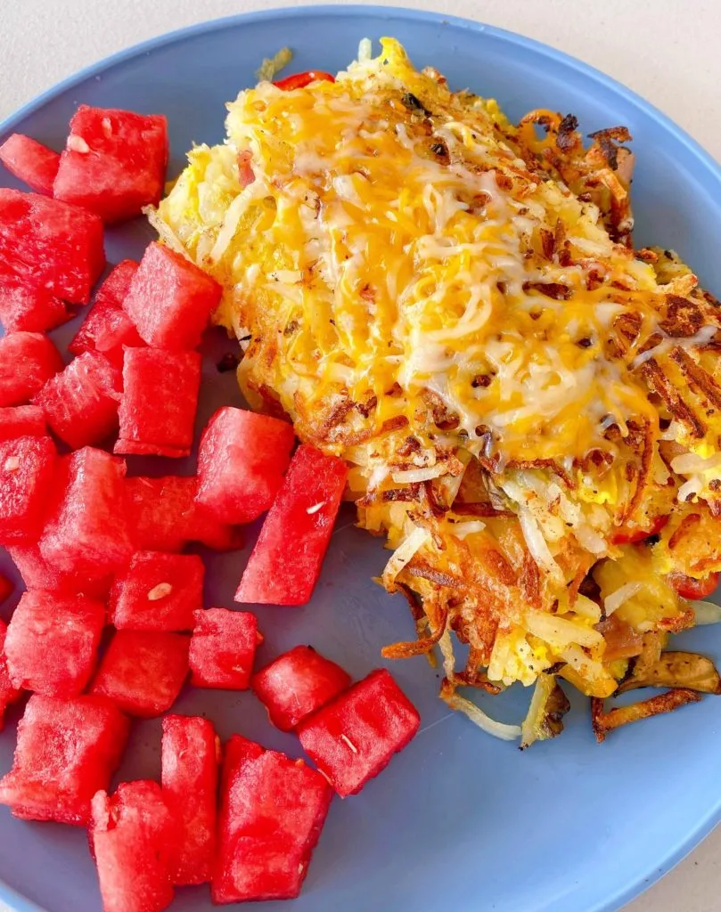 Breakfast Loaded Hash Brown Grilled  Omelet on a plage with fresh cut up watermelon.