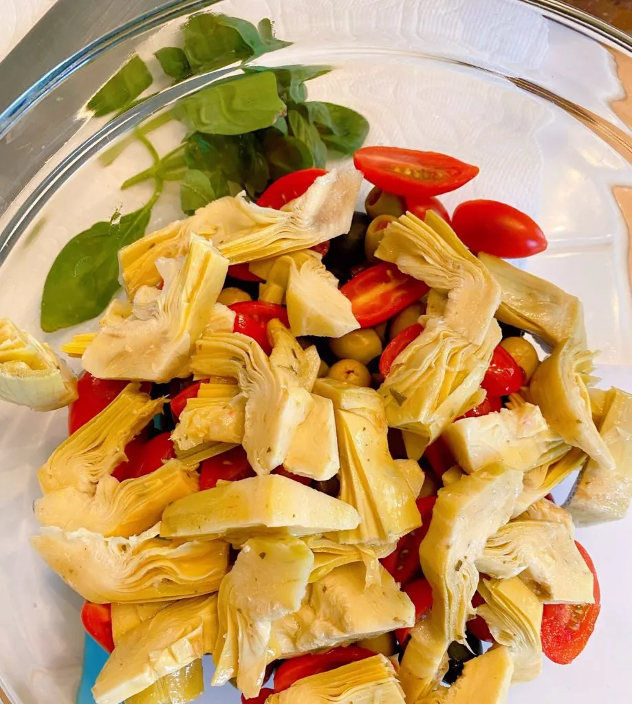 Addition of marinated artichoke hearts in the bowl with olives and tomatoes.