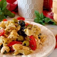 Muffuletta Olive Pasta Salad close up photo on a white plate with fresh basil surrounding it.