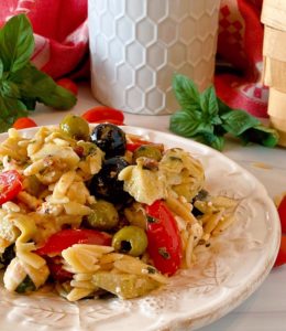 Muffuletta Olive Pasta Salad close up photo on a white plate with fresh basil surrounding it.