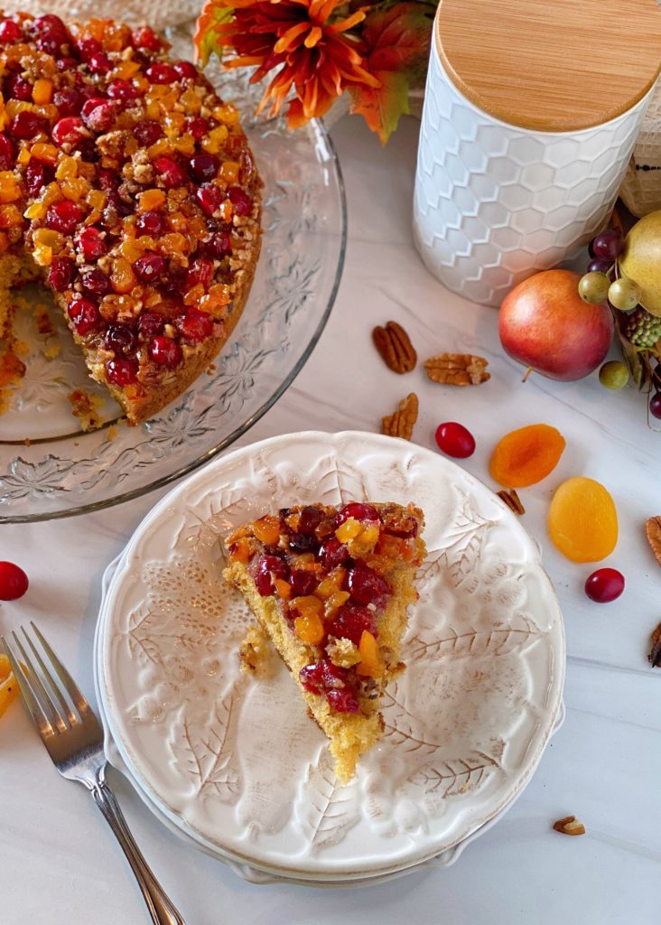 Cranberry Upside Down Coffe Cake slice on a white plate with the entire cake in the background.