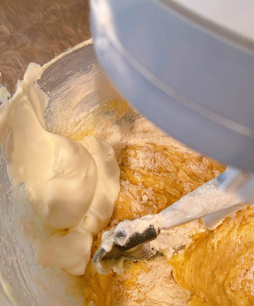 Alternating dry ingredients with sour cream for cake batter in mixing bowl.