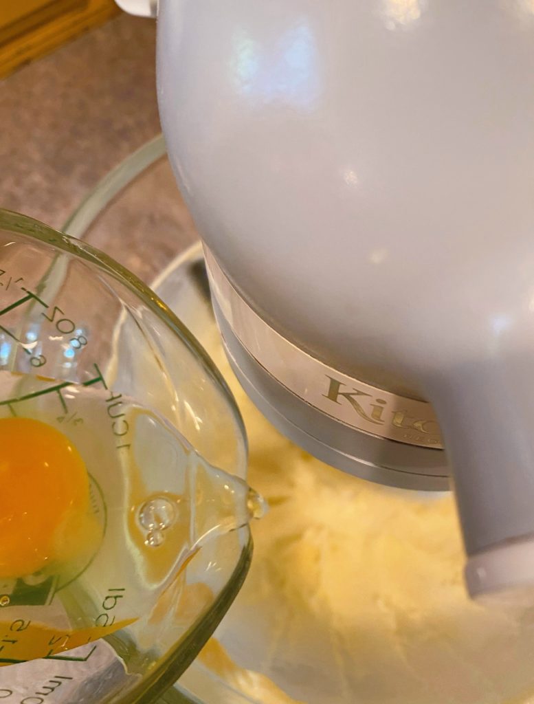 Adding eggs one at a time to butter and sugar mixture for cake.